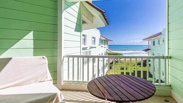 A balcony with a view of the ocean, a wooden table, and a cushioned chair. - Affordable Apartment With Ocean View (Sosúa)