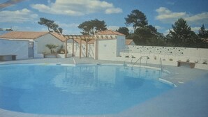 Ein Pool mit Fliesen, einer Pergola und ein weißes Gebäude mit einem Ziegeldach.