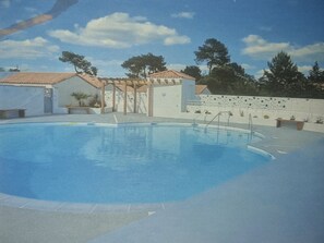 Ein Pool mit Fliesen, einer Pergola und ein weißes Gebäude mit einem Ziegeldach.