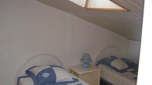 Ein Schlafzimmer mit zwei Betten, einem Nachttisch, einer Lampe und einer schrägen Decke.