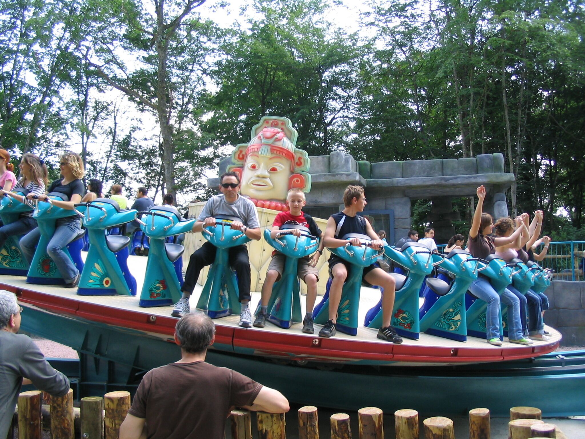 A ride with multiple seats, each seat has a handle, and there is a large decorative structure in the background.