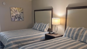 Ein Hotelzimmer mit zwei Betten, einem Nachttisch mit Lampe, einem Bild an der Wand und einer Deckenleuchte.