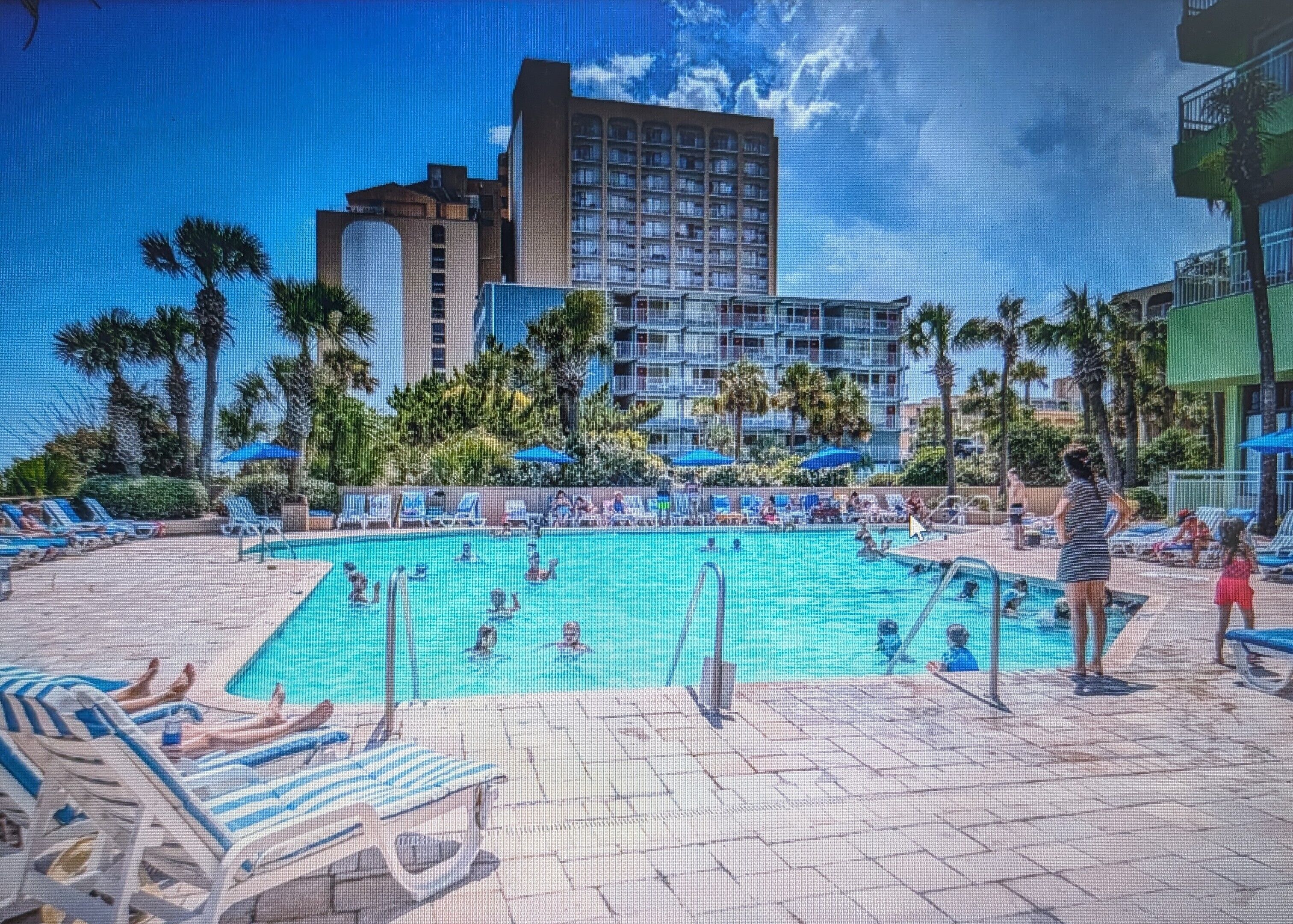 A hotel pool area with lounge chairs and a large building in the background.