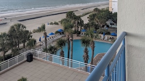 Ein Balkon mit Blick auf einen Strand, ein Schwimmbad und Palmen.