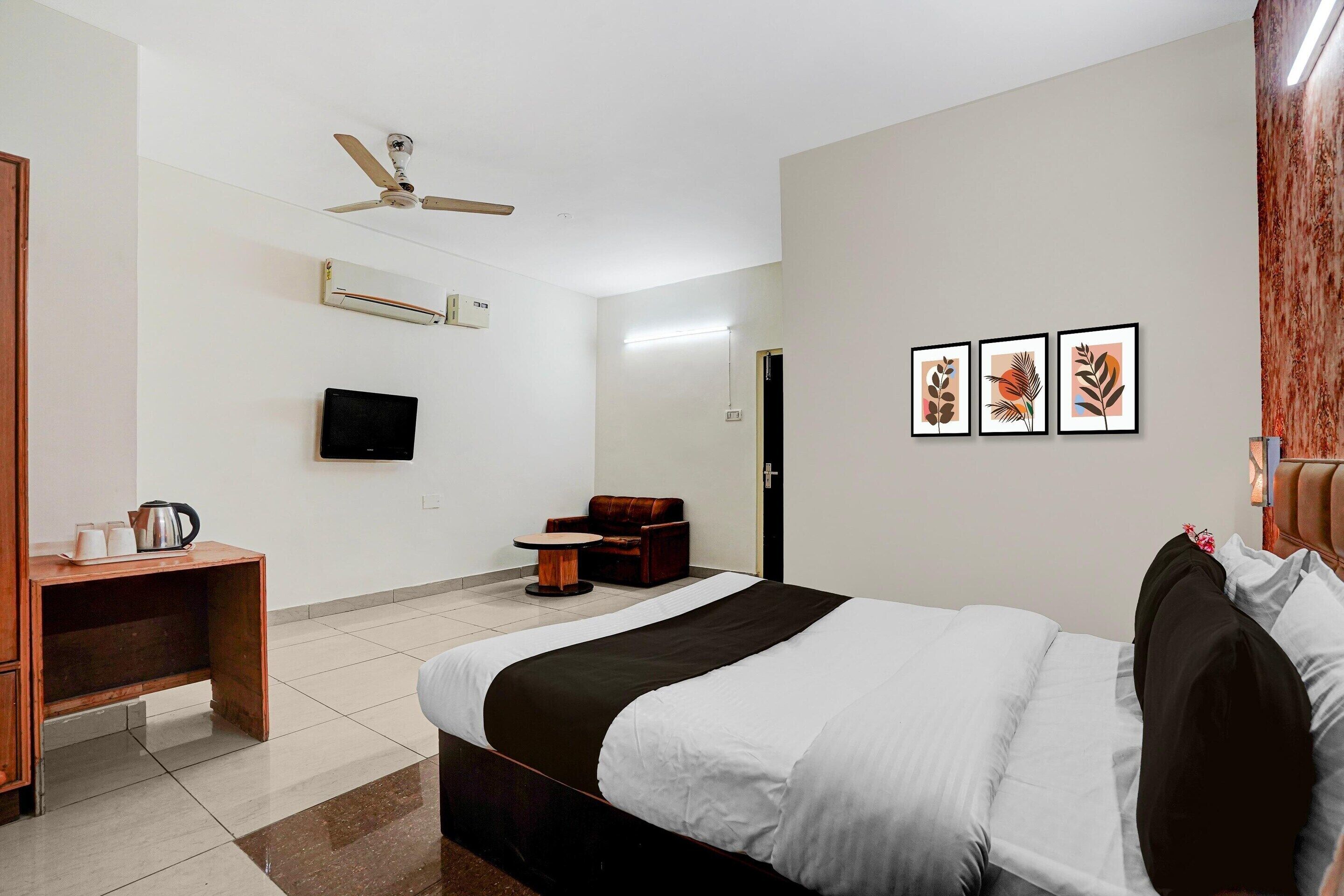 A hotel room with a bed, a desk, a chair, a TV, and artwork on the wall.