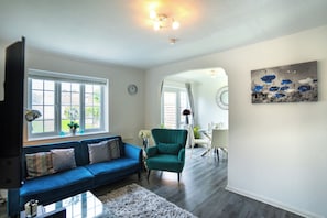 Ein Wohnzimmer mit einem blauen Sofa, einem türkisfarbenen Sessel, einem weißen Teppich und einem Bild an der Wand.