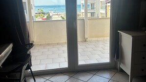 Ein Zimmer mit einer Schiebetür zu einem Balkon mit Blick auf das Meer und Gebäude.