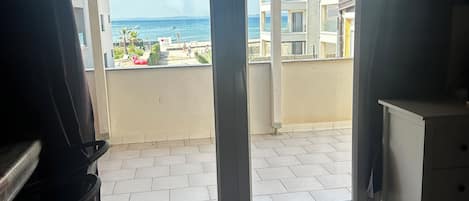 A room with a sliding glass door leading to a balcony with a view of the sea and buildings.