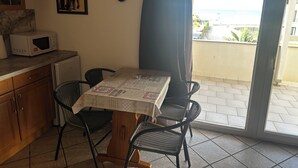 Ein Essbereich mit Tisch, Stühlen, einer Mikrowelle, einem Kühlschrank, einer Uhr und Meerblick durch eine Schiebetür.