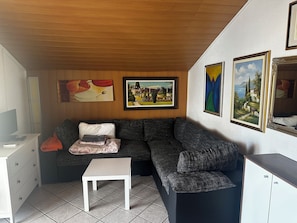 A living room with a sofa, a small table, and a cabinet. There are paintings on the wall.