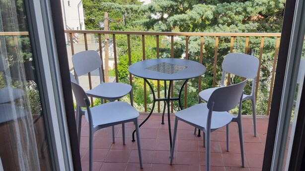 A balcony with a table and four chairs, a view of greenery, and a building in the background. - Two bedroom apartment with private parking, close to the beach and a sea (Selce)