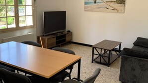 A living room with a wooden table, chairs, a TV, a sofa, and a beach-themed painting.