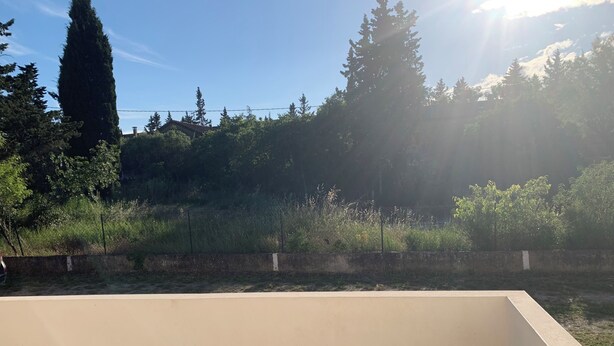 A balcony with a concrete floor, a low wall, and a view of trees and a fence.