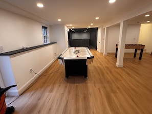Una habitación amplia con mesa de fútbol, mesa de billar y un sofá de color oscuro.