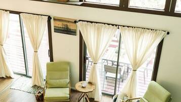 A room with a wooden staircase, a chandelier, a bull sculpture, and large windows with curtains.