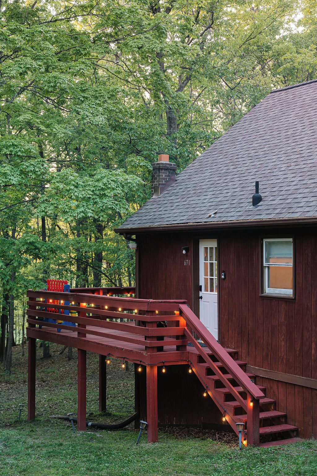 A wooden cabin with a porch, a chimney, and a number '671' on the door.