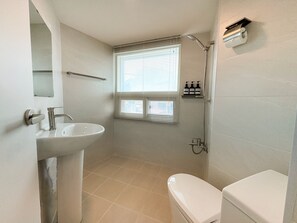A bathroom with a sink, toilet, shower, and window with blinds.