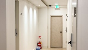 A hallway with a fire extinguisher, an emergency exit sign, and a door. - Amoon stay (Busan)