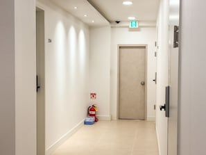 A hallway with a fire extinguisher, an emergency exit sign, and a door. - Amoon stay (Busan)