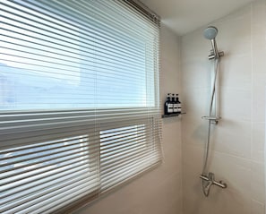 A bathroom with a shower, a window with blinds, and a shelf with toiletries. - Amoon stay (Busan)