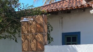 Une maison avec une colonne ornée de carreaux de céramique, une fenêtre bleue et un petit arbre dans la cour.