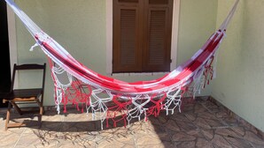 Un hamac est suspendu entre deux murs, près d’une fenêtre et d’une chaise.