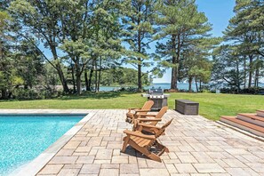 A poolside area with Adirondack chairs, a grill, and a view of a lake. - St. Michaels Waterfront Home with Pool (Saint Michaels)