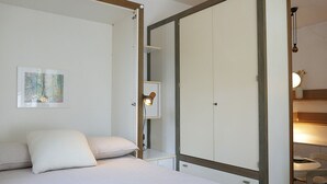Una camera da letto con un letto, un armadio, un comodino con una lampada e un quadro appeso al muro.