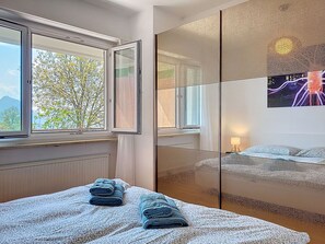 Ein Schlafzimmer mit Bett, einem Fenster mit Blick auf Bäume, einem Spiegel und einer Wand mit einer Dekoration.