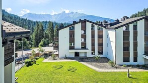 Ein modernes Gebäude mit flachem Dach, umgeben von einer gepflegten Rasenfläche und einer Bergkulisse.