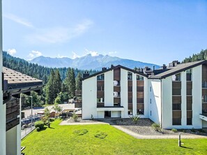 Un edificio moderno con techo plano, rodeado de un césped cuidado y montañas al fondo.