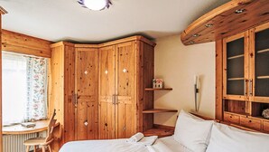 Ein Schlafzimmer mit Bett, Holzschrank, Schreibtisch mit Stuhl und einem Fenster mit Vorhängen.