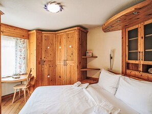 Un dormitorio con cama, armario de madera, escritorio con silla y ventana con cortinas.