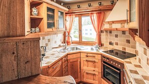 Eine kleine Küche mit Holzausstattung, einem Einbauofen, einem Herd und einem Fenster mit Vorhängen.