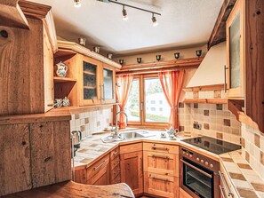 Cocina compacta con armarios de madera, horno empotrado, placa de cocina y ventana con cortinas.