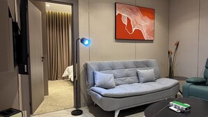A modern living room with a grey sofa, a black coffee table, a painting on the wall, and a door leading to another room. - 306 Tara-jre 2bedroom at Jabal Al Lweibdeh (Amman)