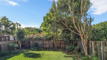 A backyard with a wooden fence, a tree, and a grassy area.