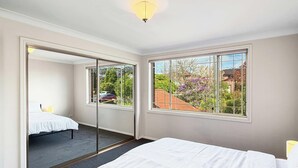Un dormitorio con cama, un ventanal grande y una puerta que da a otra habitación.