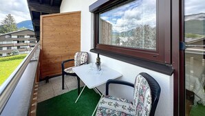 Un balcon avec une table et deux chaises, un panneau en bois et une vue sur une montagne.
