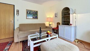 Un salon avec un canapé, une table basse en verre, une lampe, une bibliothèque et une porte.