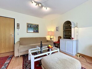 Ein Wohnzimmer mit einer Couch, einem Glastisch, einer Lampe, einem Bücherregal und einer Tür.