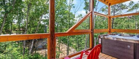 Una terraza de madera con un jacuzzi, sillas rojas y vistas a árboles.