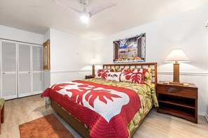 A bedroom with a bed, two bedside tables, a nightstand, a ceiling fan, a wall-mounted painting, and a wardrobe. - Keauhou Punahele C103 2 Bedroom Condo (Kailua-Kona)