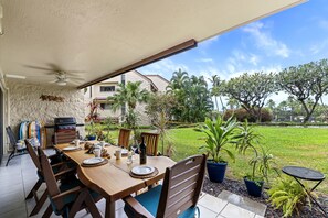Ein Essbereich im Freien mit einem Tisch für vier Personen, umgeben von Stühlen, einem Deckenventilator und einem Grill.