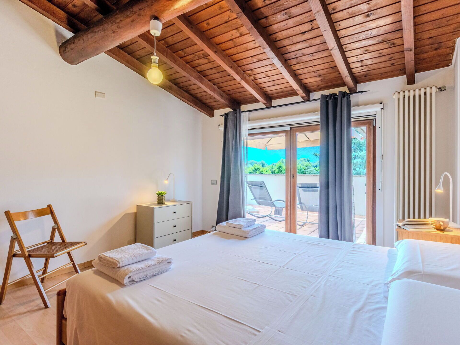 Um quarto com cama, uma cadeira, mesa de cabeceira, abajur e vista para o exterior.
