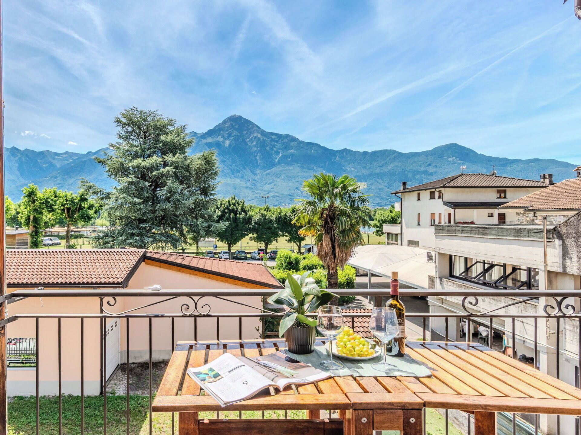 A balcony with a table set for dining, a view of mountains, and a building with a tiled roof.