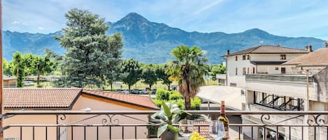 A balcony with a table set for dining, a view of mountains, and a building with a tiled roof.