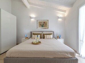 Ein Schlafzimmer mit Bett, Nachttischen, einer Lampe, einem gerahmten Bild und einem Fenster.
