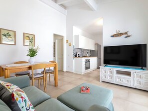 Ein modernes Wohnzimmer mit Sofa, Esstisch mit Stühlen, Küchenzeile und Fernseher.