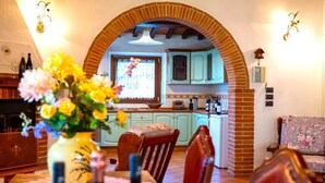Un comedor con un arco de ladrillo que da a la cocina, una mesa con un florero y un sofá con tapicería floral.